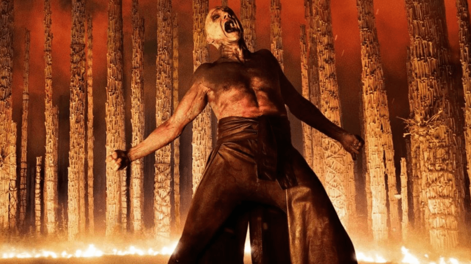 A figure stands with arms outstretched in front of a wall of fire in a dark forest in '28 Years Later: The Bone Temple'.