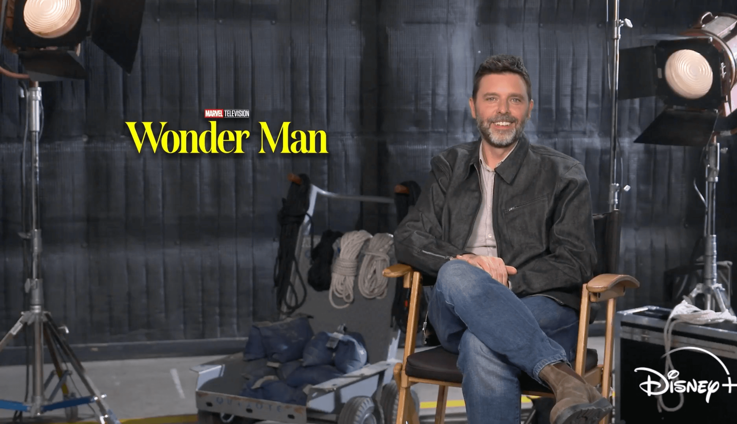 'Wonder Man' writer Andrew Guest sits for a remote video interview in front of a Disney+ 'Wonder Man' backdrop.