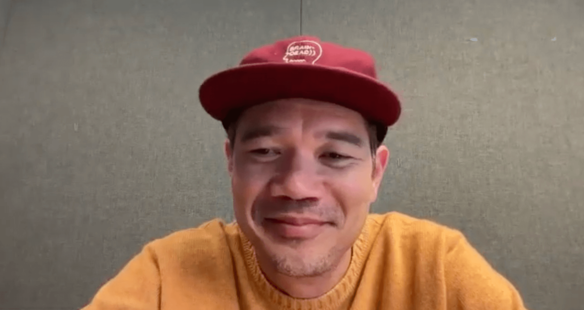 'Wonder Man' director Destin Daniel Cretton smiles during a video interview wearing a yellow shirt and red cap.