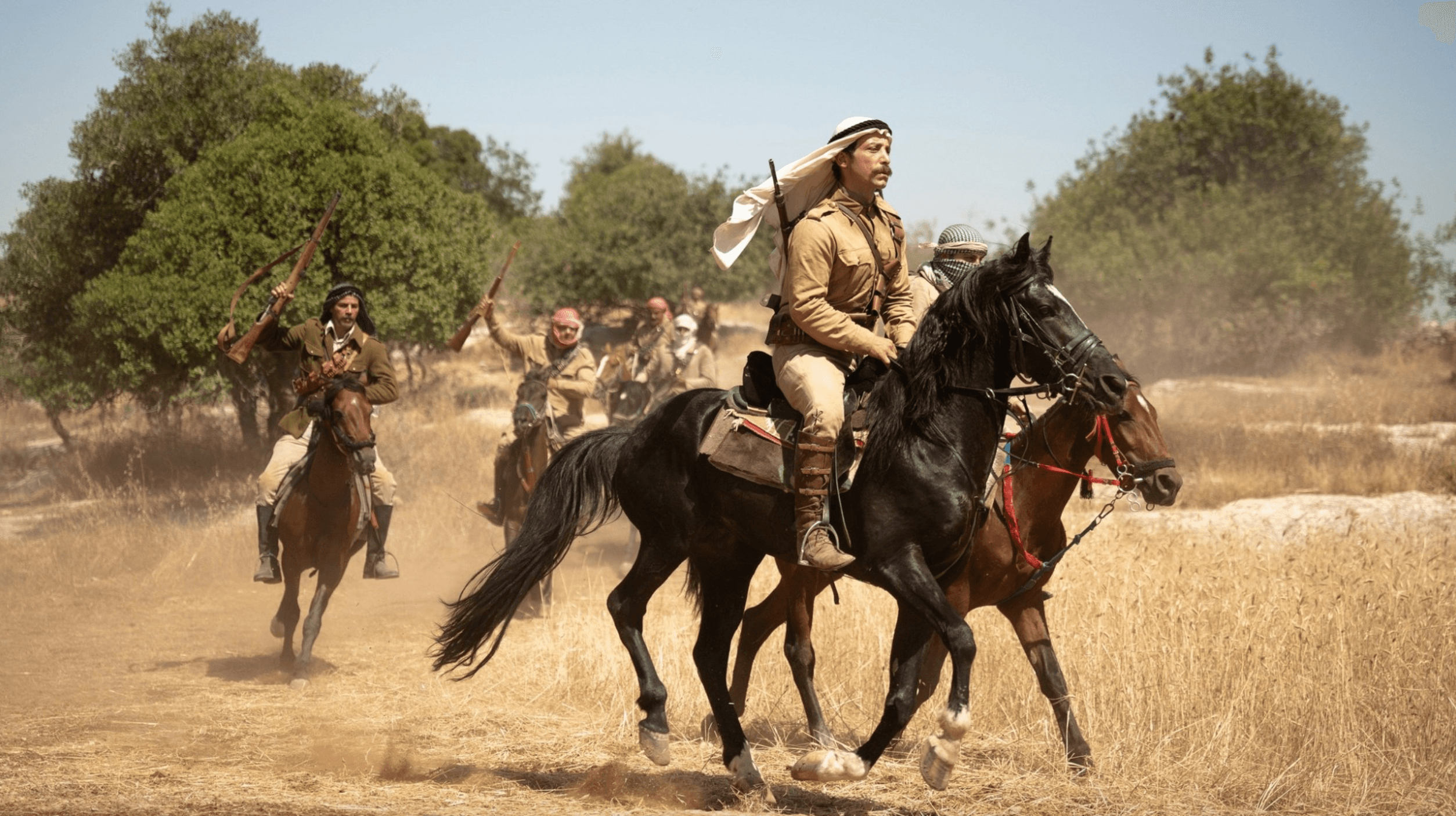 Mounted soldiers in period uniforms ride across a dusty field in a scene from 'Palestine 36'.